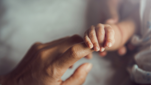 Close-up image of a tiny baby's fingers holding onto a woman's index finger