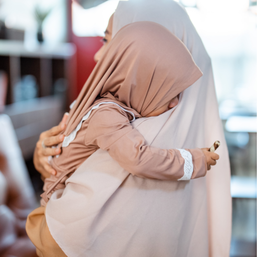 A woman in a light pink hijab holds a young child in her arms