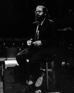 Black and white photo of Allen Ginsberg on a stool