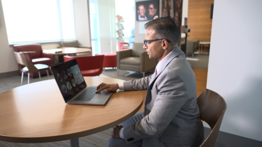 A man is sitting at a round table in a medical office, looking at black and white images on his laptop computer 