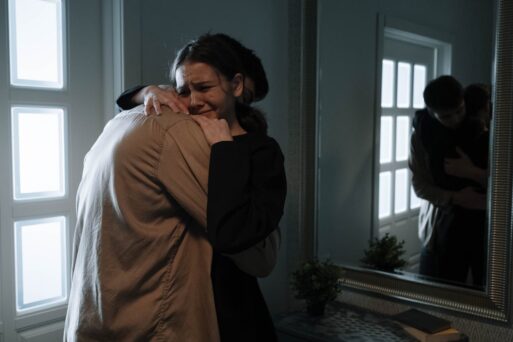 A grieving couple hugs before a mirror.