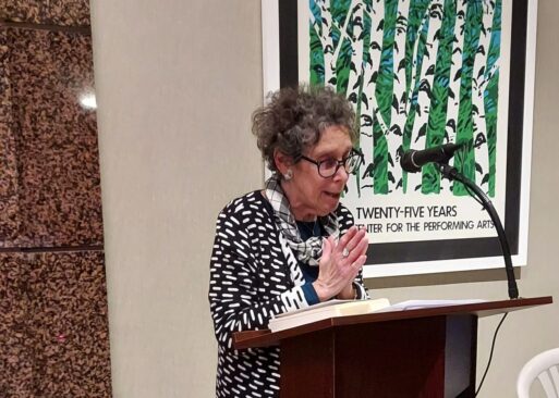 Jan Seskin giving a reading at a podium.