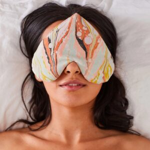 Woman lying down under a heart-shaped eye pillow 