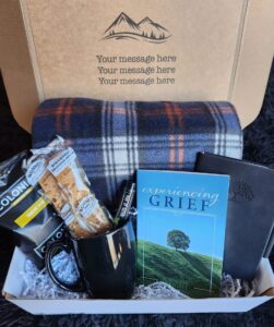 A box with plaid blanket, mug, snacks, and books