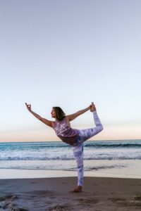 Profile view of woman in dancers pose (yoga) on the beach, supporting healthy aging