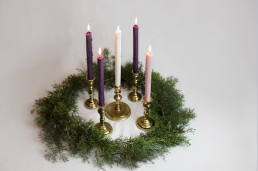 A wreath of cedar garland surround five light candles in brass candlesticks