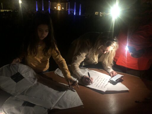 Woman writes a message on a lantern under phone light. 