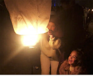 Child looks on in wonder as woman warms sky lantern at The Lights Fest