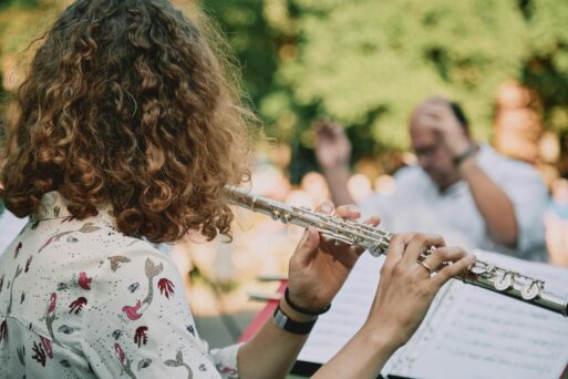 We are looking at a woman with shoulder-length curly hair facing away from us as she plays the flute in an orchestral performance