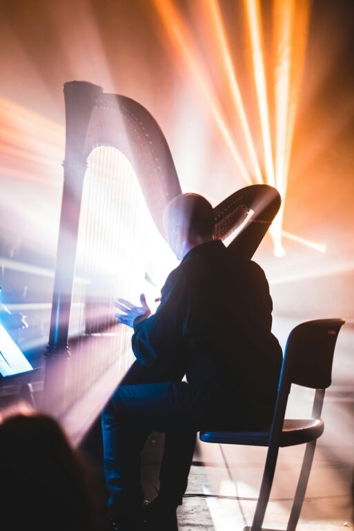 A person playing the harp is dramatically backlit, creating an aura of light around the instrument and musician