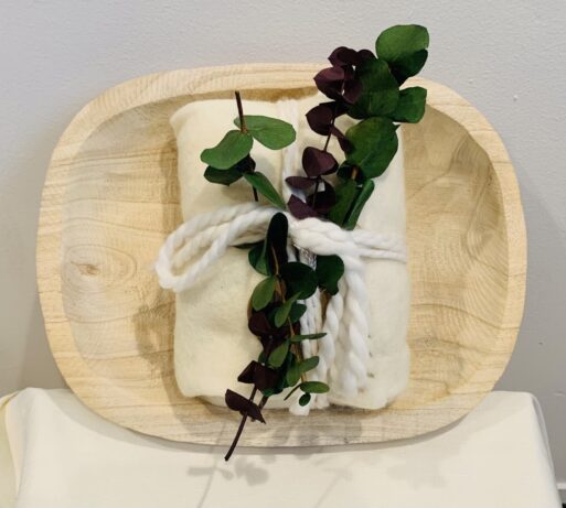 Burial shroud sitting in wooden tray with green leafy branch tied to it. 