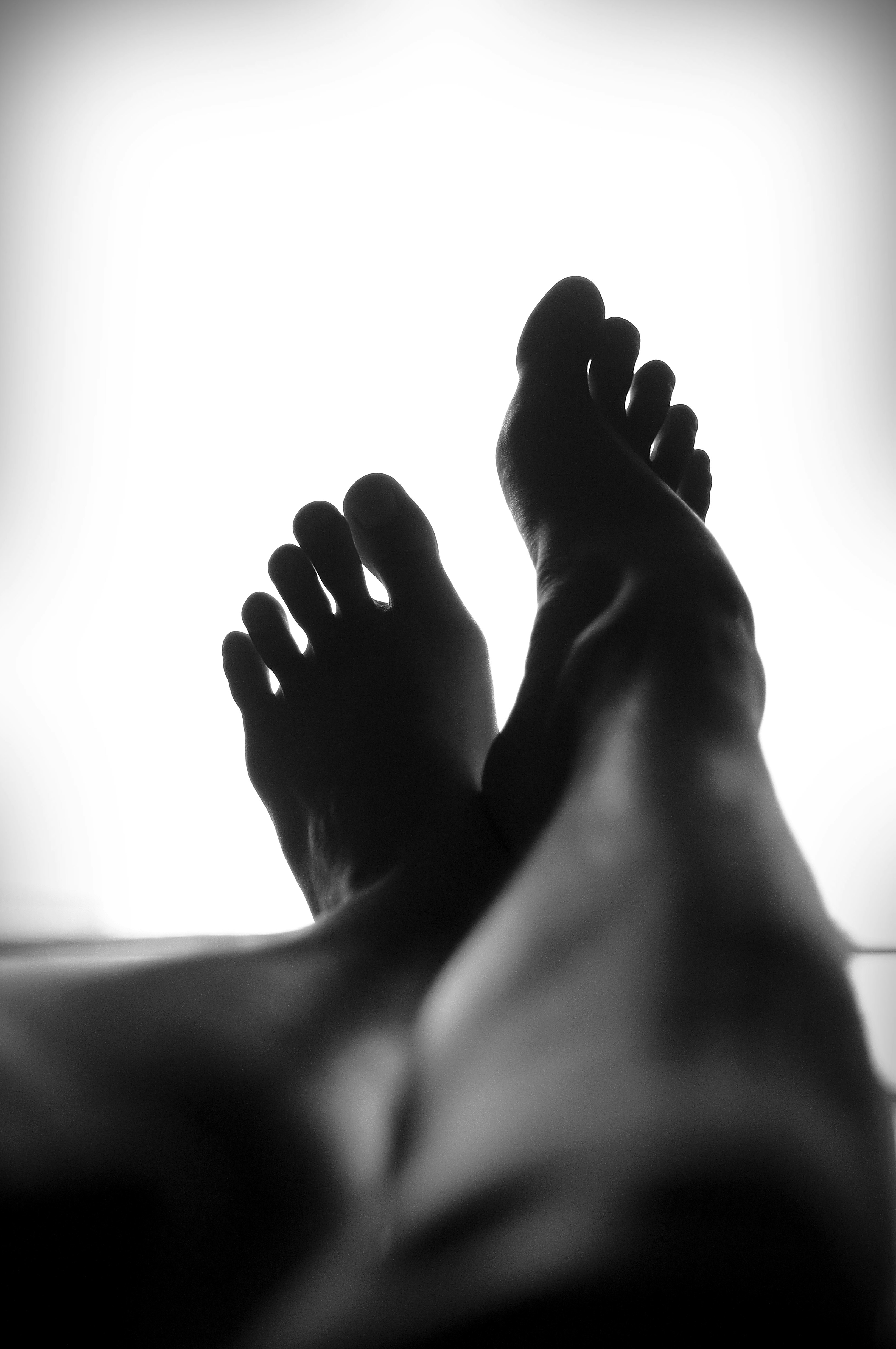 A black-and-white image from the perspective of someone laying down, looking at their feet. Beyond the feet is just a vast, white space.