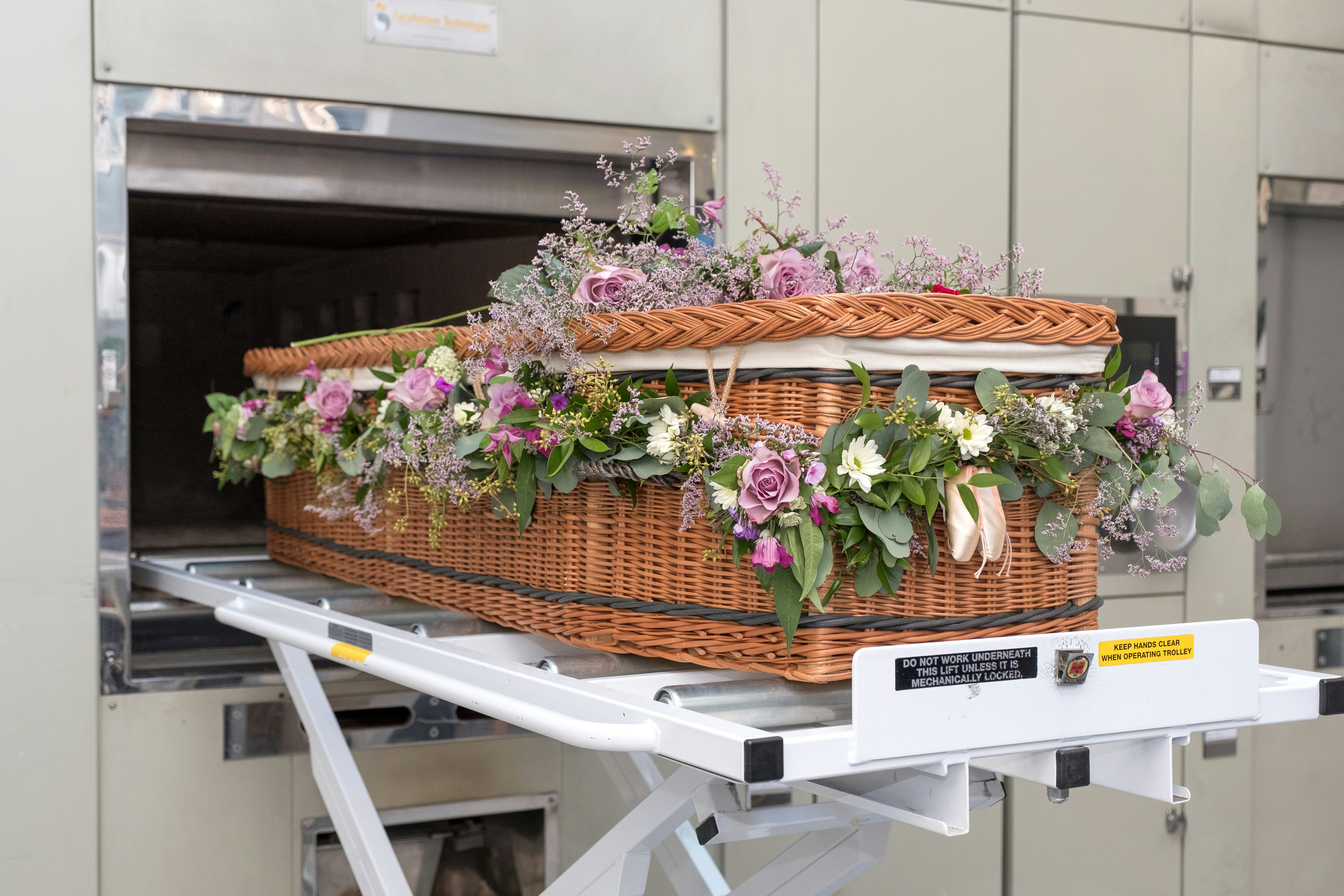 A casket made of wicker and embellished with flowers is sitting on a table in a cremation facility.