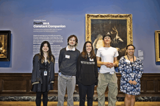 Five teenagers stand in front to exhibit wall. 