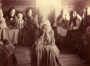 A woman sits with her head in her hands surrounded by other women. Archival photograph