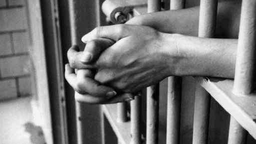A black-and-white photograph of an inmates' hands clasped through the bars of their cell.