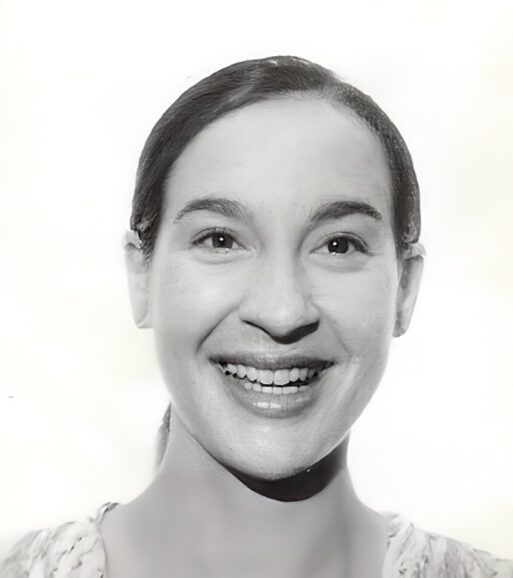 A black and white image of a smiling woman with dark brown hair pulled into a low ponytail, from the shoulders up
