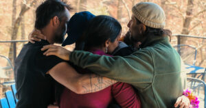 A circle of people huddles close with their arms around each other. 