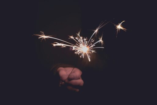 A hand dimly lit holds a sparkler in the darkness