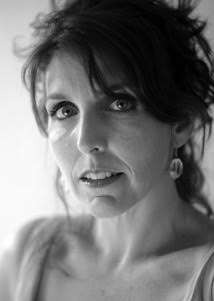 A black and white headshot of a woman with long brown hair in an informal updo looks right at the camera.