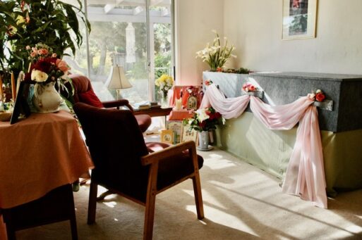 A coffin draped in pink fabric and flowers sits next to a homemade altar in someone's home.