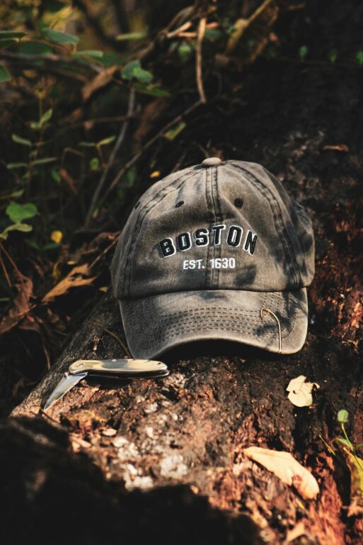 A gray Boston Red Sox baseball hat and a pocket knife on a log in the woods to be included in a cremation ceremony.