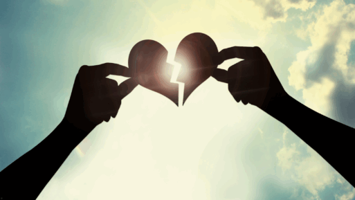 Silouetted against a cloudy-but-sunlit sky, two hands are holding pieces of a broken heart as if they're trying to fit them back together