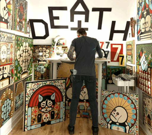 artist Mike Egan stands with his back to the viewers in front of a collection of his artwork