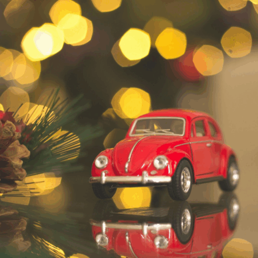 A red toy car is next to a holiday garland, with Christmas lights in the background as part of a memorial service keepsake.