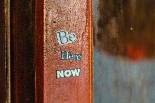 A sign on a wall reads "Be here now," an important message when moving on from loss.