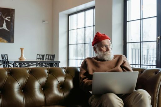An elderly man sits on his computer on a couch, rather than engaging in daily exercise.