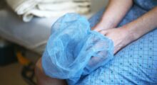 A person sits on a hospital bed holding a disposabel cap