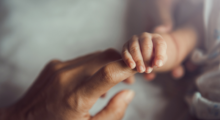 Close-up image of a tiny baby's fingers holding onto a woman's index finger