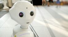 A cute robot looks at the camera with blurry people in background