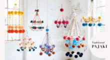 Several bright, colorful chandeliers made from paper flowers and streamers hang from the ceiling in a bright, white room