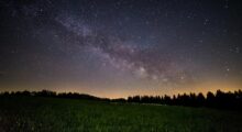 a beautiful night sky pictured above lush green grass and a glowing horizon.