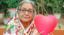 Aurora Levins Morales sits in a yard holding up a pink heart.